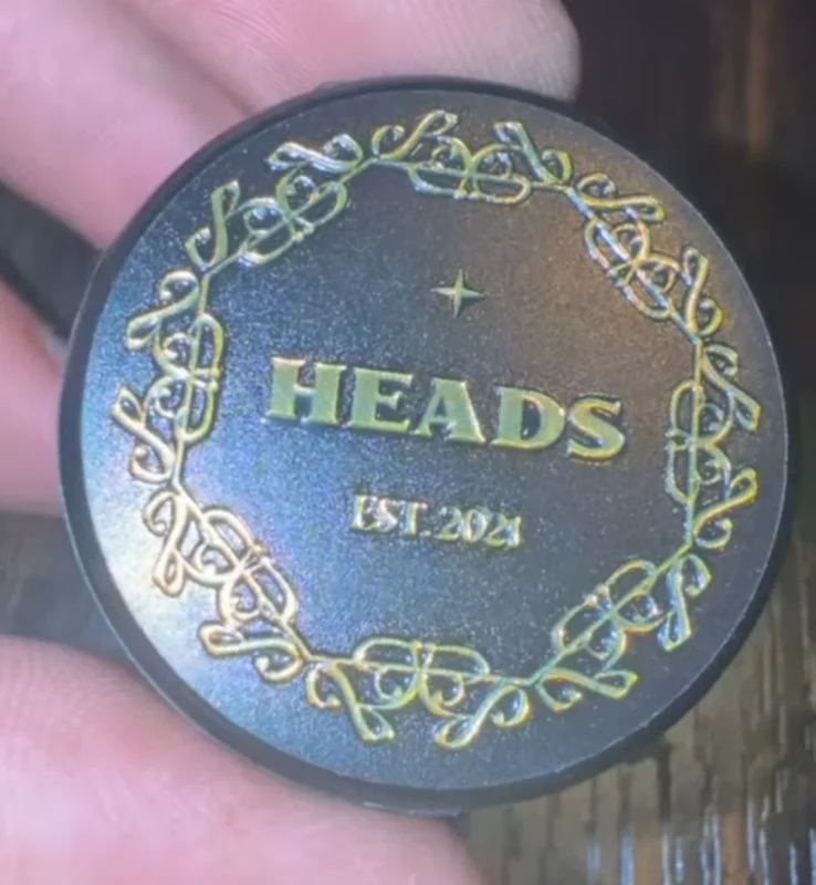 A HEADS Est. 2021 jar lid with an ornate gold border